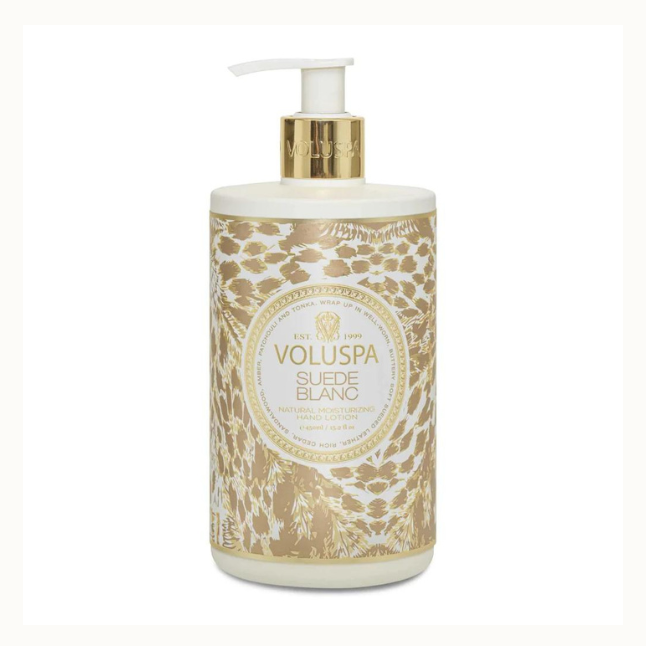 Product photograph by Voluspa of a Suede Blanc hand lotion bottle on a white background featuring the iconic brand logo, an intricate tan animal print pattern, and a metallic gold pump collar