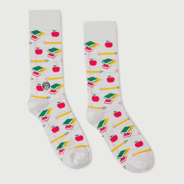 A pair of printed crew socks by BD showcasing a school-themed pattern on a neutral background, featuring vibrant red apples, yellow pencils, and stacks of green and red books over a faint notebook-lined design