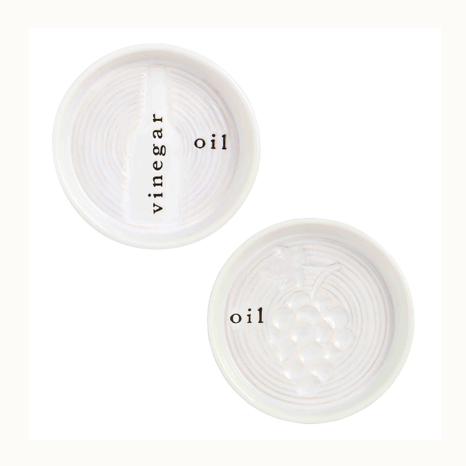 Ceramic stoneware bread dipping dishes for oil and vinegar featuring embossed bottle and grape cluster motifs with textured concentric circular ridges and black serif typography against a white background
