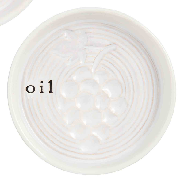 Ceramic oil dipping dish showcasing an embossed bunch of grapes in the center with textured concentric rings and the word oil in a black serif font on a cream-colored glaze